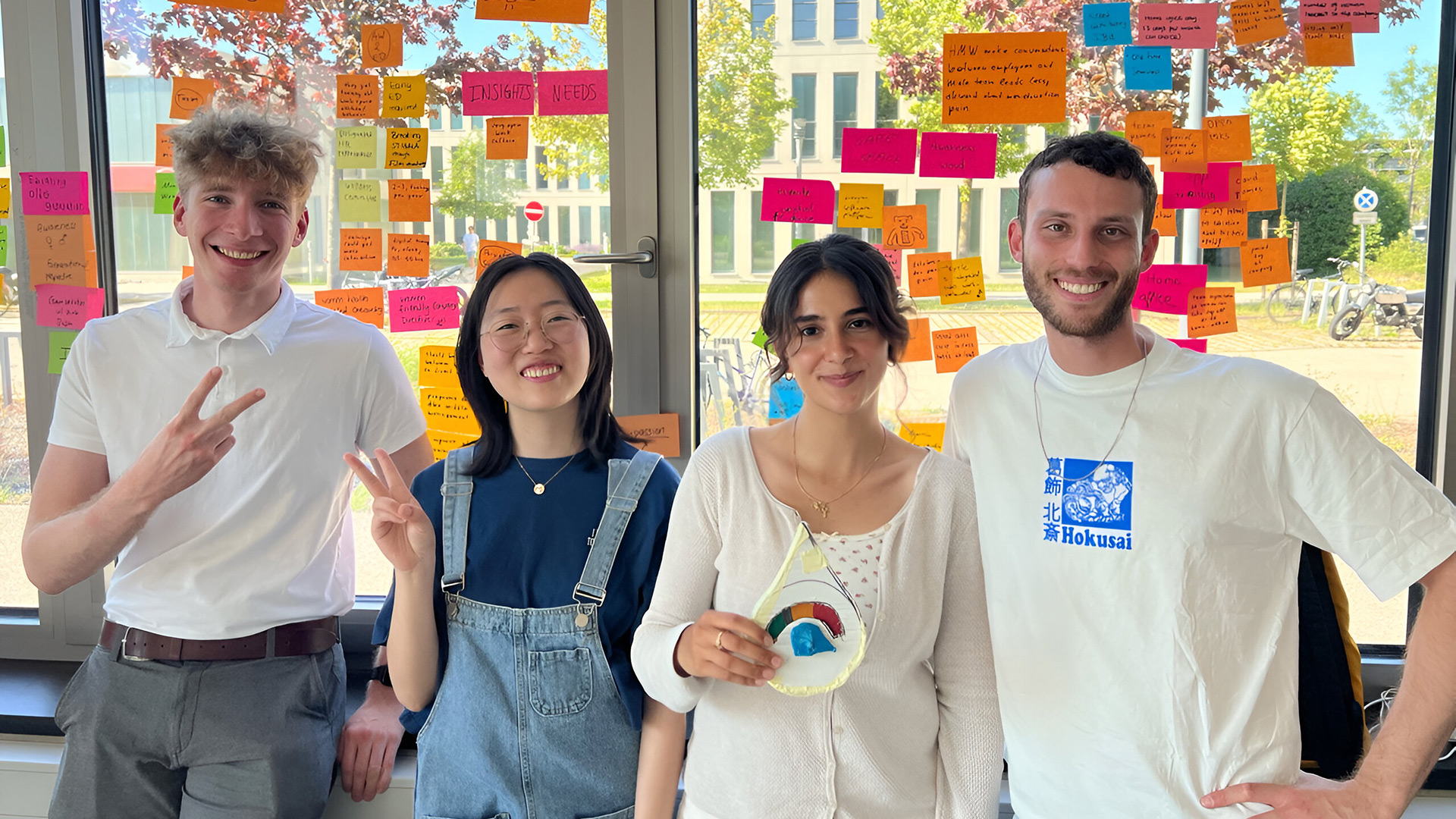 Four stundents in front of a window pasted with post-its.