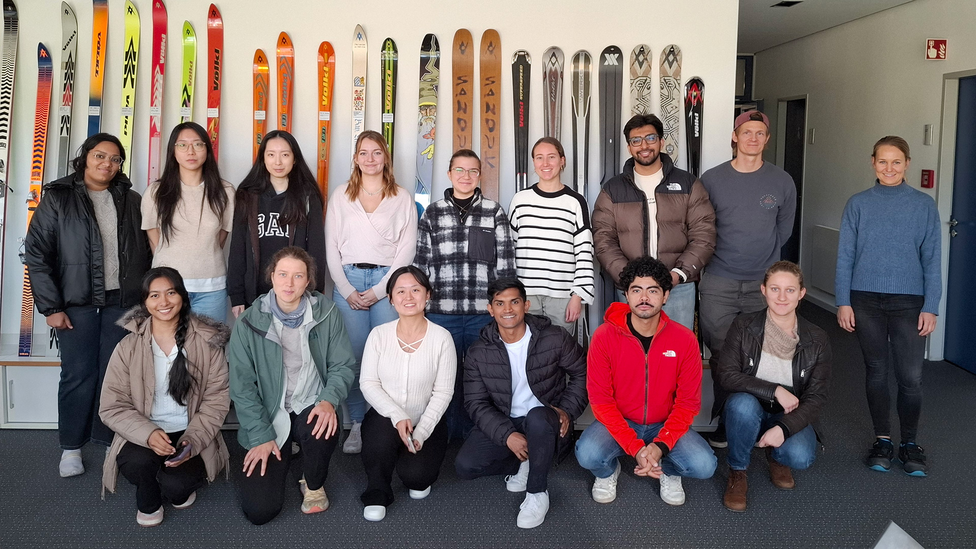 A group of students in front of a wall with a lot of colorful skis.